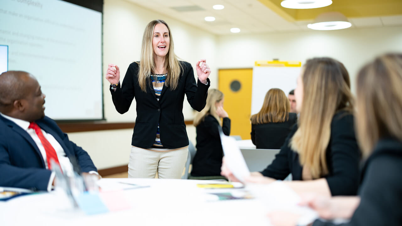 a woman speaks to 3 people sitting at a table, blurred in the foreground